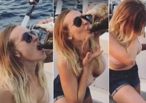 Mulher bebe cerveja direto da boca de peixe morto