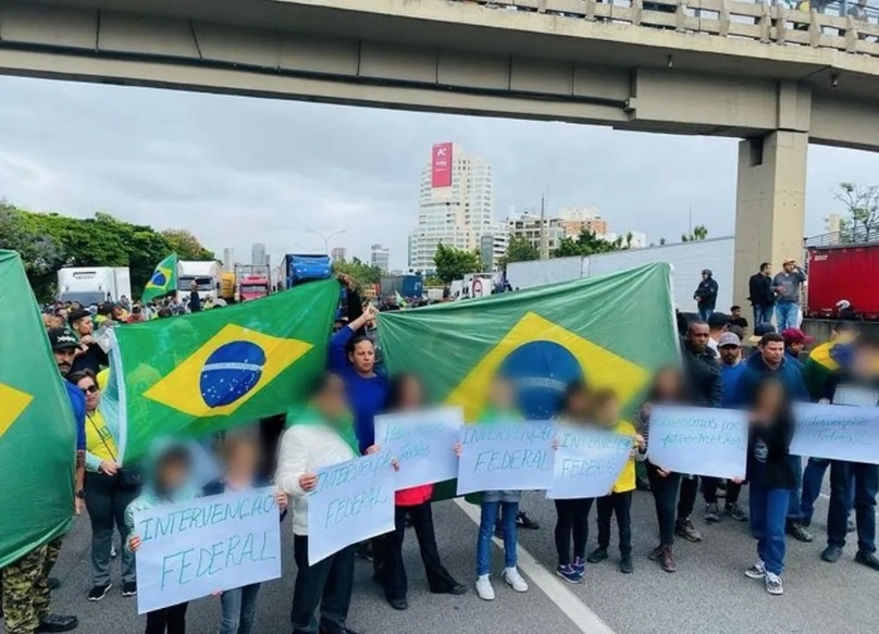 Crianças segurando cartazes são colocadas à frente de bloqueio de rodovia