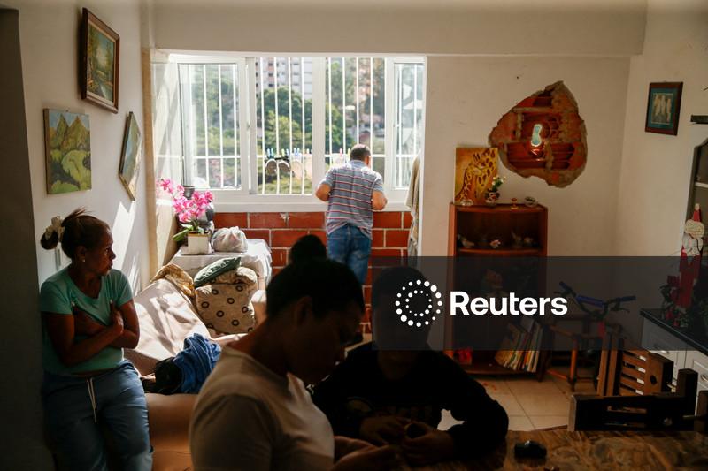 Pessoas sentam-se dentro de uma casa onde uma parede foi perfurada por um fragmento de foguete, após os EUA lançarem um ataque contra a Venezuela